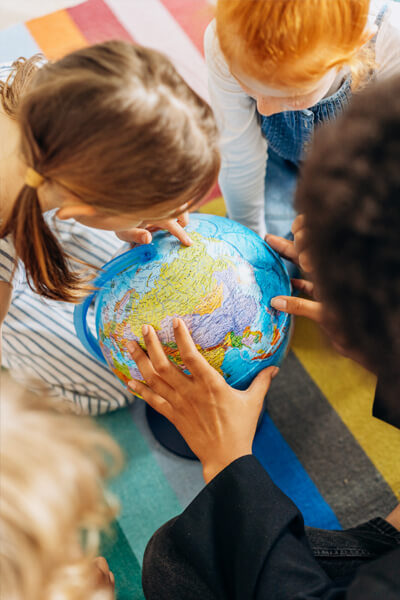 Photograph looking over the shoulder of a teacher as kids look and point at a globe