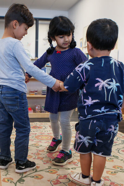 A trio of children at varying ages standing in a circle holding hands