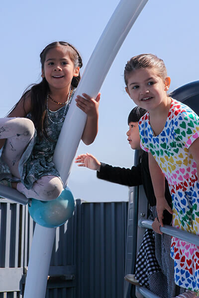 A trio of girls outdoors playing on the jungle gym
