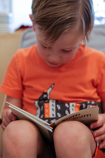 Young boy in orange shirt seated in chair reading a book