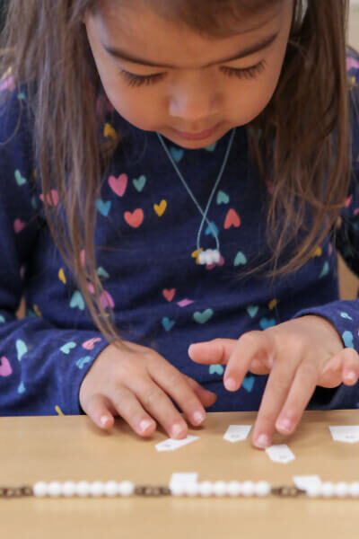 Young girl sitting at desk looking down using set of white golden beads conducting mathematics