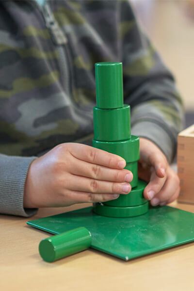 close up of young boy in camouflage long sleeve shirt stacking varying size and shaped green wooden blocks