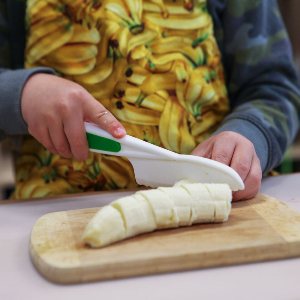 Close up of young child holding child safe plastic knife cutting a banana