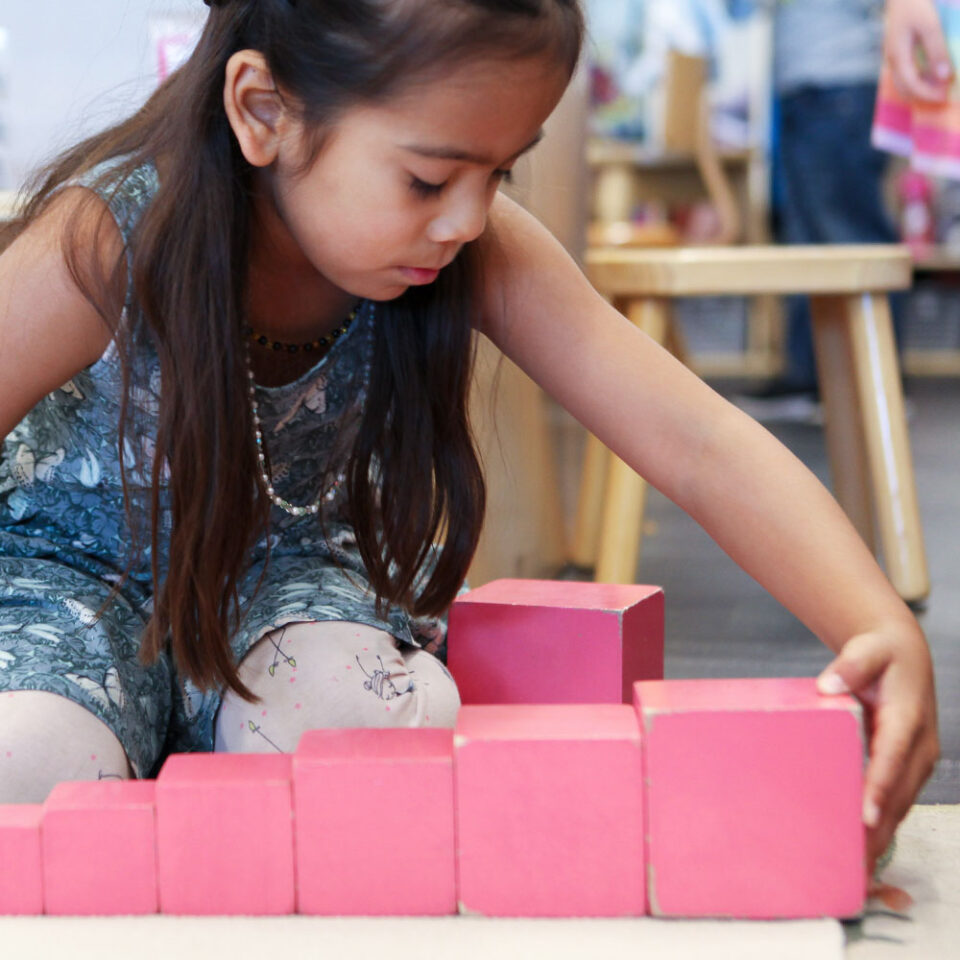 Young girl sitting on floor playing with Montessori pink tower blocks
