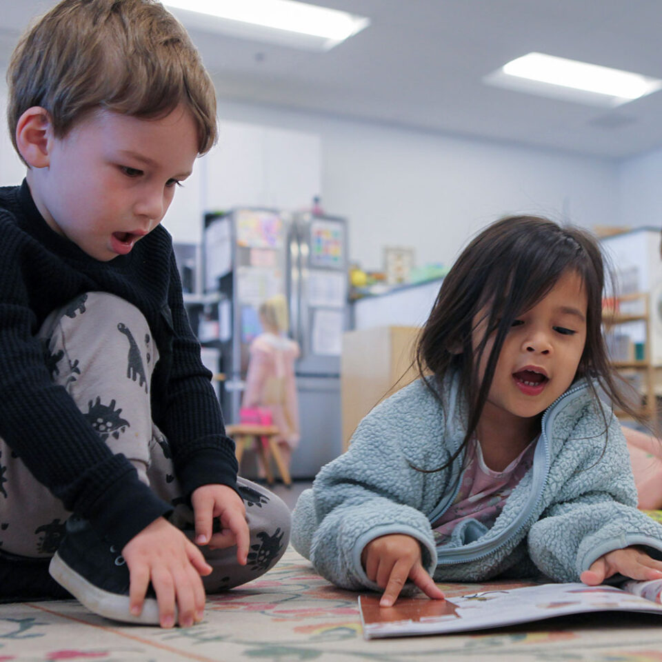 Photo of young boy and girl sitting on the floor reading a book together