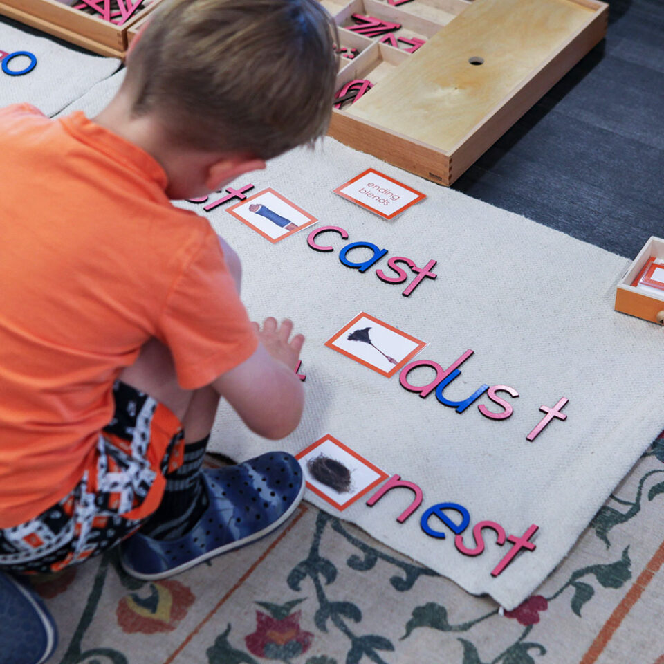 Young blond hair boy in orange shirt leaning forward using moveable alphabet to spell out words