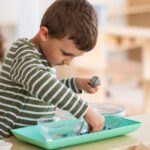 Photo of young boy standing at table with two bowls holding a metal tea strainer