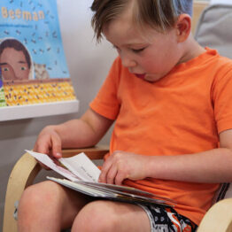 Young caucasian boy in orange shirt seated and reading a book